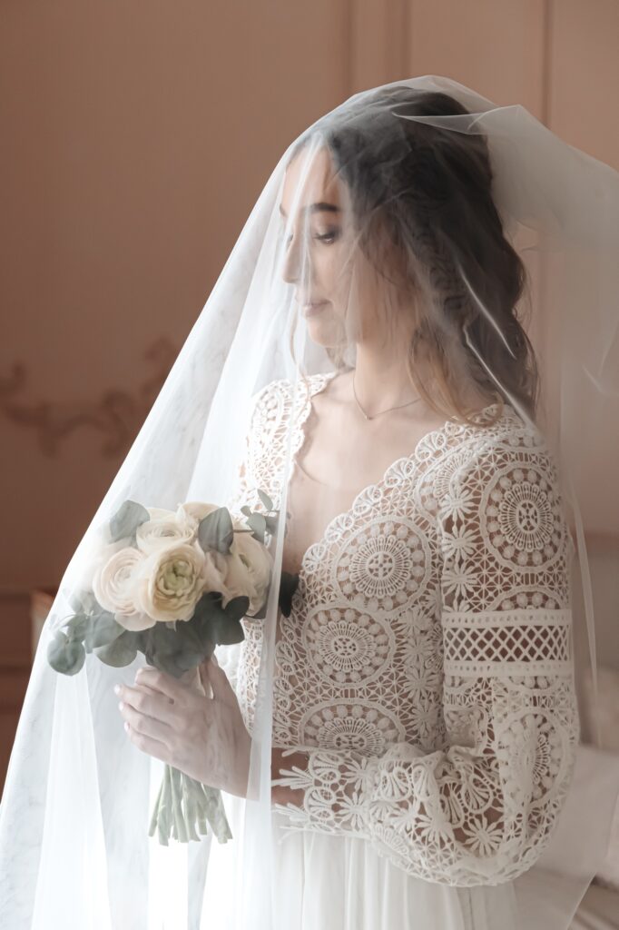 Portrait of a young bride covered with a wedding veil holding a bouquet.